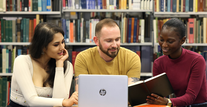 Three students sat together around a laptop in the library