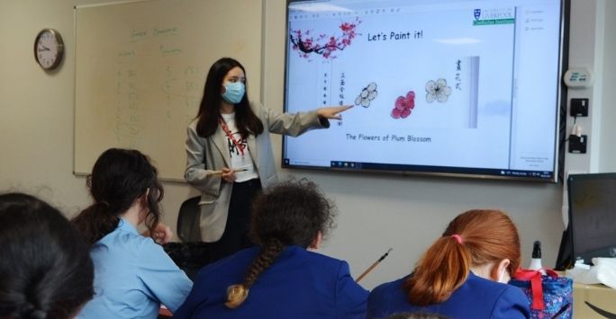 Photo of a tutor pointing at a whiteboard whilst teaching students.