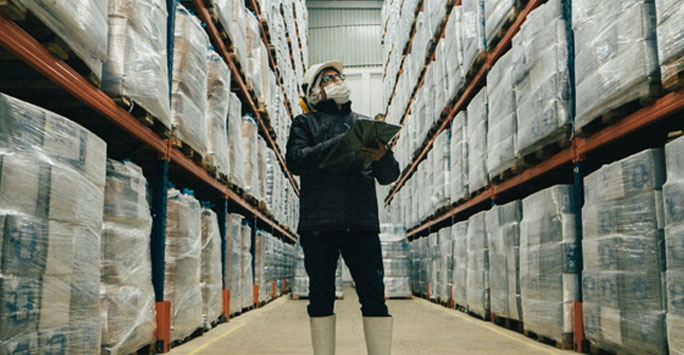 Person wearing a mask between warehouse shelves