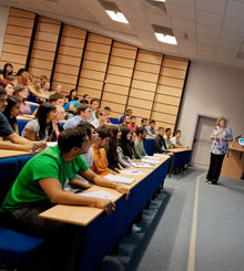 A number of dental student sitting in the school lecture theatre having a lecture delivered by a female member of staff standing at the front of the lecture theatre