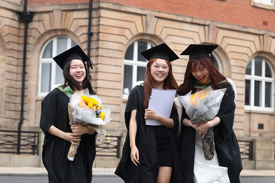 Three students wearing graduation cap and gowns and holding flowers