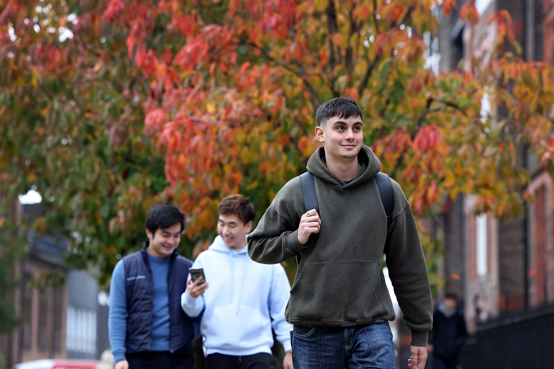 A student walks through the University of Liverpool campus, with two other students in the background