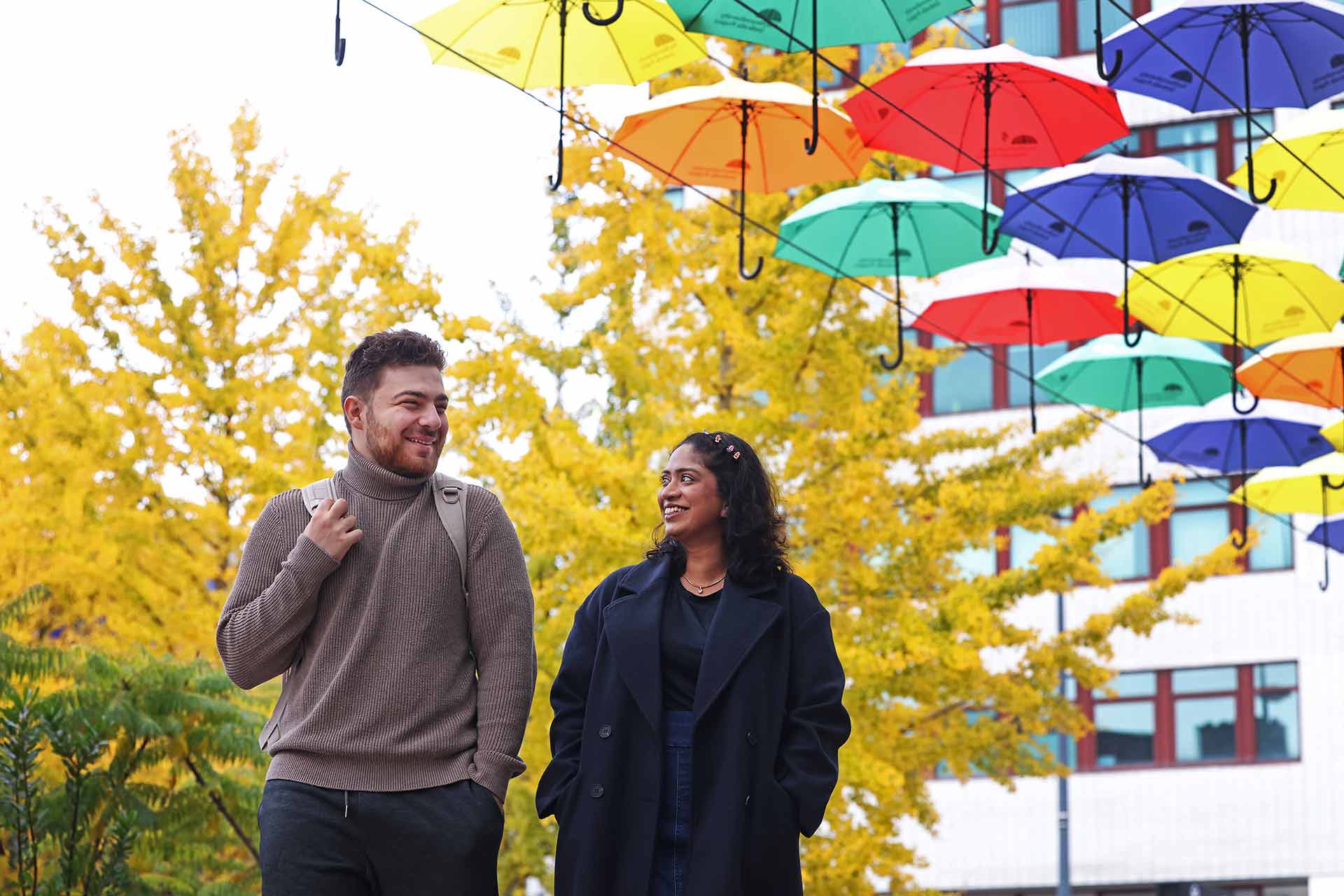 Two students walking underneath an umbrella display on the University of Liverpool campus