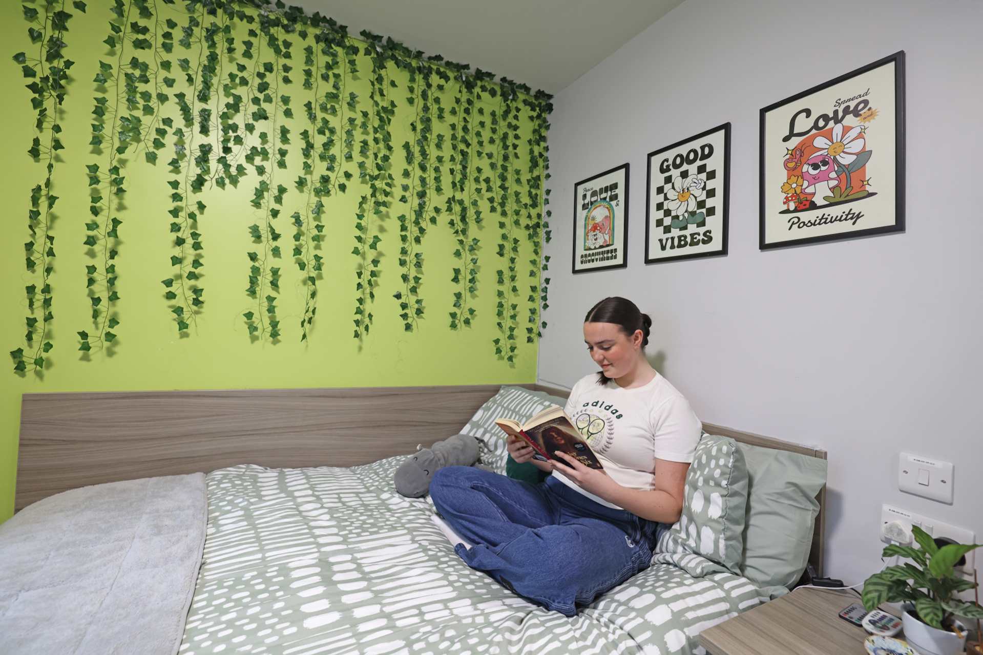 A student sits on her bed reading a book in University accommodation.