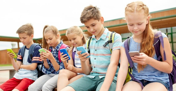 A group of five children sat in a line, all looking at their mobile phones.