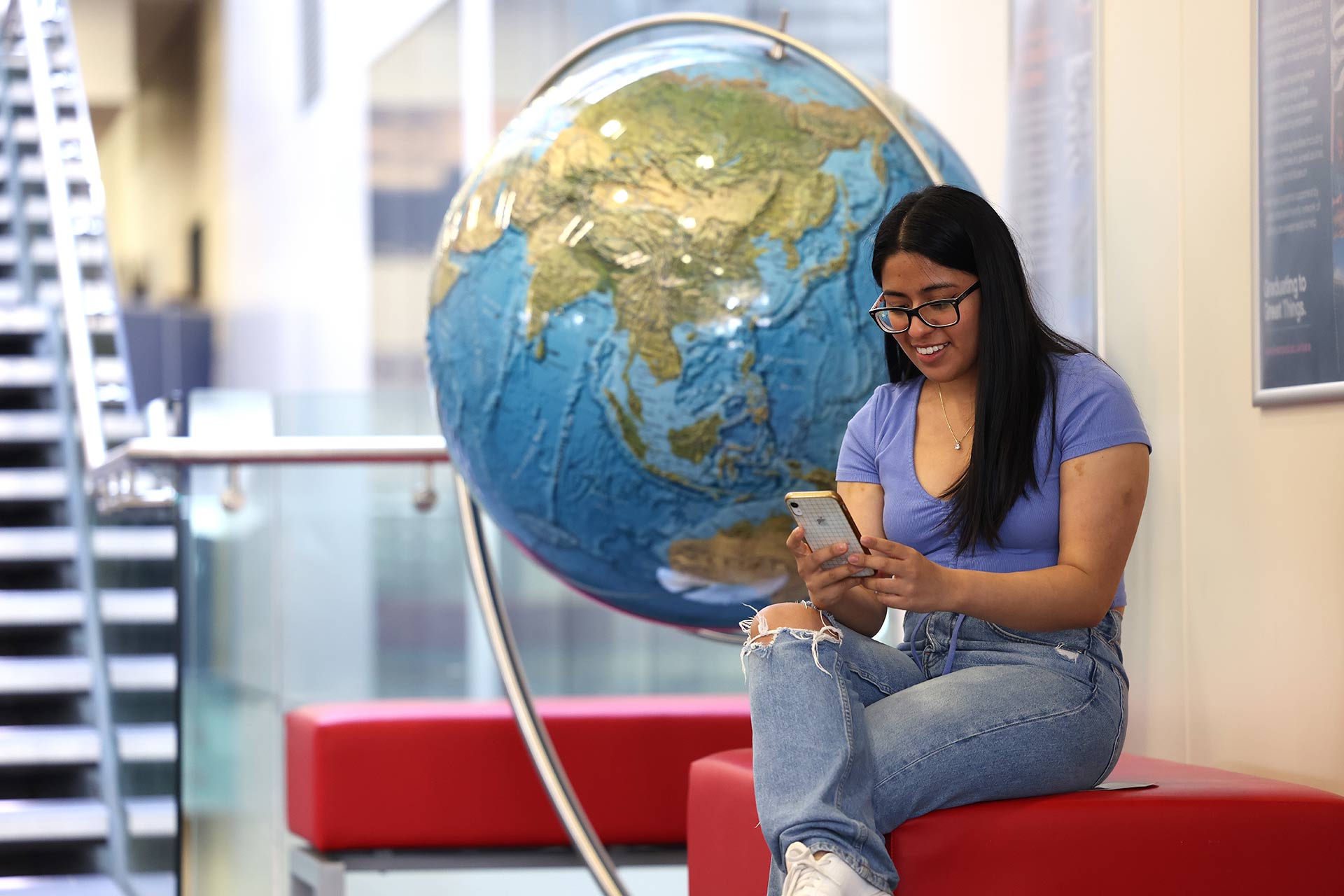 Student sits on a bench in front of a large colour model of the globe